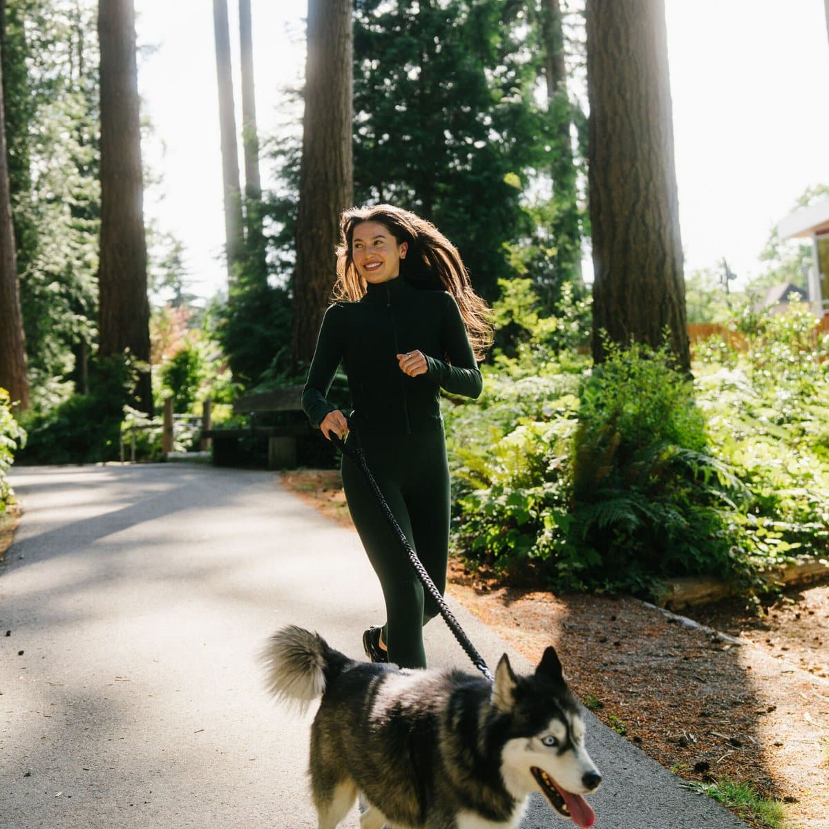 Woman running with her husky on a forest trail at leləm̓ Forest Park