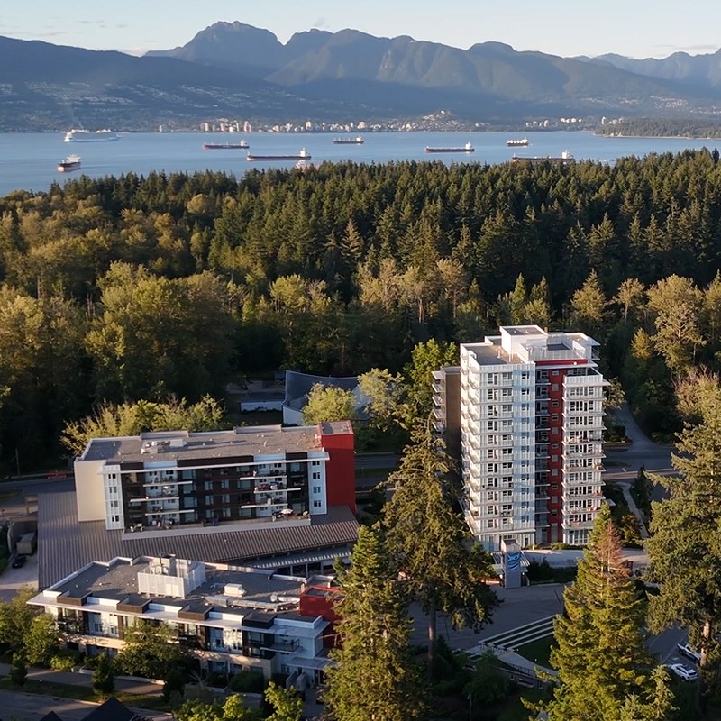 Aerial view of leləm̓ village with Pacific Spirit Park, the ocean and mountains